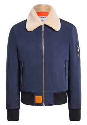 Veste de bombardier marine avec un col en fourrure crème, fermeture éclair sur le devant, poignets côtelés et une étiquette orange en bas de l'ourlet. Tissu lisse et structuré.