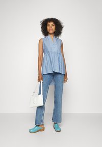 Top sem mangas riscado em azul e branco com decote em V, bainha peplum, combinado com jeans flare azul claro e tamancos com sola de madeira. Bolsa branca.