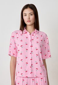 Camicia rosa a maniche corte con motivo a righe, decorata con motivi di ciliegie rosse e gambi verdi, colletto a bottoni e vestibilità rilassata.
