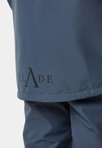 Niebieski materiał wierzchni o gładkiej fakturze, z wyraźnym czarnym logo "SLADE" blisko dolnej krawędzi. Prosty design z czystymi liniami.