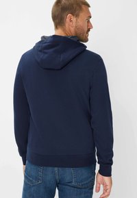 Felpa con cappuccio blu navy con coulisse e una texture liscia, caratterizzata da un rivestimento interno grigio a contrasto e polsini e orlo a costine. Vestibilità casual.