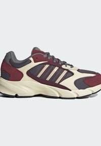 Zapatilla deportiva en color marrón y gris, hecho de materiales de malla y ante, con tres rayas reflectantes, suela acolchada y detalles texturizados.