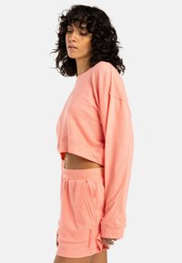 Korte lichtroze sweatshirt met lange mouwen en een losse pasvorm, gecombineerd met bijpassende geplooide shorts met een koord in de taille.