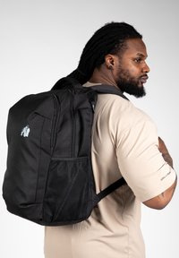 Zwarte rugzak van duurzaam materiaal, voorzien van een mesh zijvak, dubbele ritscompartimenten en een kenmerkend logo op het voorpaneel.