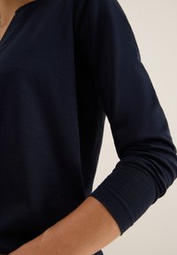 Mörkblå långärmad skjorta med uppkavlade ärmar, som visar personens underarm mot en neutral bakgrund.