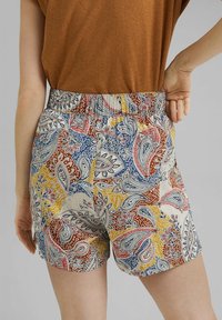 Pantalones cortos coloridos con estampado de paisley y cintura elástica en tonos rojo, azul, amarillo y crema, hechos de tela ligera.