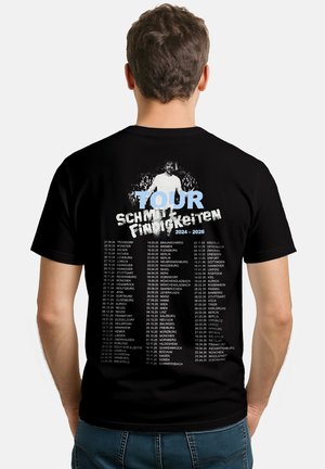 Uomo che indossa una maglietta nera del tour elencando le date delle città del 2024-2026 sotto il testo blu "TOUR Schmitts Eindrücken" con una piccola figura bianca sopra.
