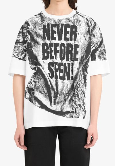 T-shirt ample blanc avec un graphique noir très visible portant l'inscription "JAMAIS VU AVANT !" et une texture froissée. Manches courtes.