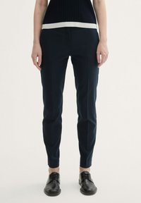 Námořnické modré kalhoty na míru vyrobené z hladké tkaniny; mají plochý přední díl, slim fit a decentní boční kapsy. Spárováno s černými botami.