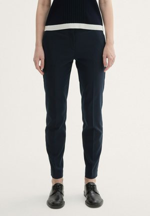 Pantaloni tagliati blu navy realizzati in un tessuto liscio; presentano un davanti piatto, una vestibilità slim e tasche laterali sottili. Abbinati a scarpe nere.