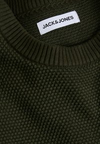 Sötétzöld, textúrázott kötött pulóver bordázott kerek nyakkivágással és fehér címkével, amelyen az "JACK & JONES" felirat található, és a gallér belső oldalába van varrva.