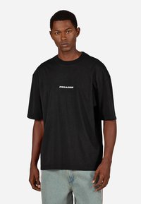 Czarny bawełniany t-shirt o luźnym kroju, krótkich rękawach i białym logo "PEGADOR" nadrukowanym na klatce piersiowej. Prosty, jednolity design.