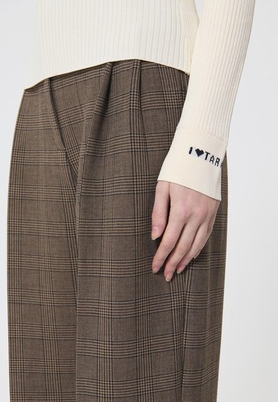 Ściągaczowy sweter w kolorze kremowym z haftem "I ♥ TARA" przy mankiecie, w połączeniu z brązowymi spodniami w kratę z wysokim stanem, z plisami i teksturowanym materiałem.