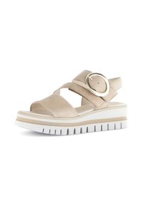 Beige mockasksandaler med korsade remmar och en stor guldspänne. Har en vit ribbad sula med beige detaljer och en bekväm plattformdesign.