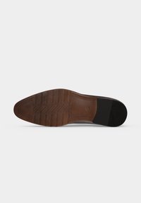Semelle d'une chaussure habillée en cuir marron avec une bande de roulement à motif et une section de talon en caoutchouc noir, montrée sur un fond clair uni.
