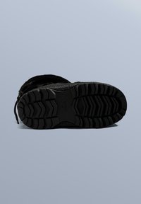 Sort vinterstøvle med tekstureret gummisål med dybe slidbaner for greb, snøredesign og blødt, pelslignende overmateriale.