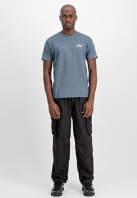 Camiseta de algodón gris con mangas cortas y un logo en el frente, combinada con pantalones cargo negros con bolsillos laterales y un corte relajado.