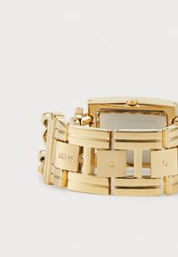 Gold stainless steel wristwatch with a rectangular face, link bracelet design, and engraved brand logo on certain links.