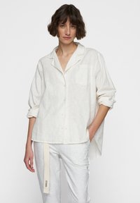 Witte linnen blouse met kraag, een enkele borstzak en opgerolde mouwen. Gecombineerd met lichtgrijze joggingbroek met een labelaccent.