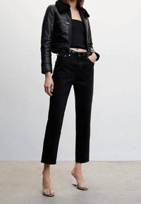 Czarna skórzana krótka kurtka z futrzanym kołnierzem, zestawiona z czarnymi, wysokim stanem i prostymi nogawkami dżinsami oraz sandałami na obcasie z przezroczystym paskiem.