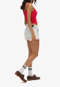 Rood geribd tanktop en lichtblauwe denim shorts met rafelige zoom. Accessoires zijn zwarte sokken met witte strepen en bruine schoenen.