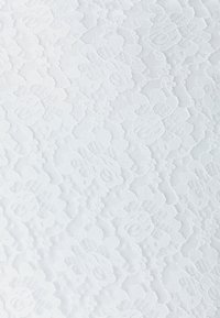 Tissu en dentelle blanche avec motifs floraux, présentant une texture délicate et un aspect légèrement transparent, mettant en valeur des détails complexes sur l'ensemble.