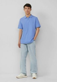 Helles blaues Polohemd aus weichem Stoff, mit klassischem Kragen und kurzen Ärmeln, kombiniert mit lockeren hellblauen Jeans und weißen Turnschuhen.