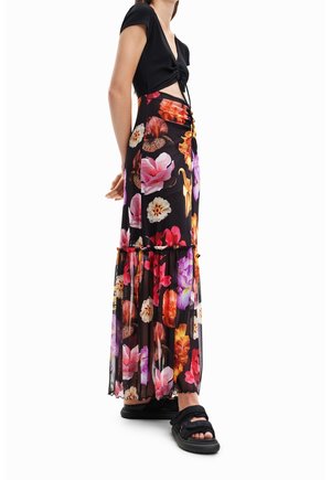 Woman wearing a black cropped top and a long black floral skirt with pink, orange, and purple flowers, paired with black sandals.