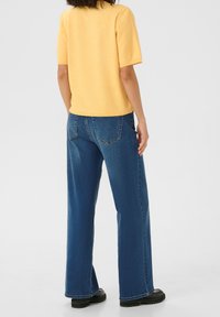 Top corto a maniche corte giallo in maglia abbinato a jeans a gamba dritta di lavaggio medio. Il look è completato da scarpe nere con suola spessa.