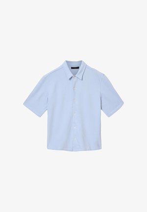 Chemise bleu clair à manches courtes avec col classique et boutons blancs, posée à plat sur un fond blanc.
