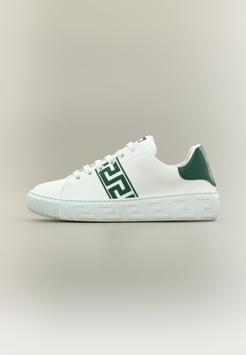 Baskets basses blanches avec une bande géométrique verte et un renfort au talon, semelle épaisse embossée d'un motif géométrique assorti, fermeture à lacets.
