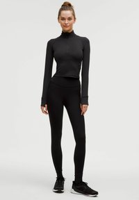 Sort, langærmet, fitted top med høj krave og kvart lynlås, parret med højtaljede sorte leggings. Begge lavet af strækbart stof.
