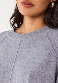 Maglione lavorato a maglia azzurro chiaro con scollatura rotonda, caratterizzato da un motivo testurizzato e maniche a raglan, realizzato in un materiale morbido e caldo.