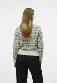 Pull en vert clair à motif Fair Isle, avec un col rond et des bords-côtes aux poignets et à l'ourlet, associé à un pantalon noir.