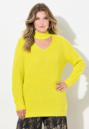 Lys gul strikket sweater med høj hals og V-formet udsnit. Lange ærmer, ribbet tekstur, falder under hoften. Sammen med mønstrede bukser.