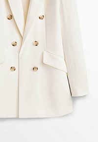 Hvid skræddersyet blazer med dobbeltradet design, guldknapper, to forlommer og en glat, struktureret stoftekstur.