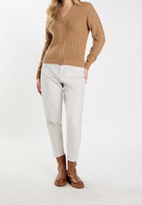 Brązowy, dziany kardigan z dekoltem w serek i trzema guzikami, w zestawieniu z jasnymi spodniami i brązowymi botkami za kostkę o teksturowanej podeszwie.