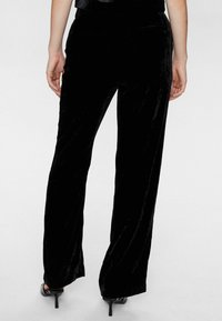 Schwarze Samt-Hosen mit weitem Bein zeichnen sich durch eine glatte Textur und einen leichten Glanz aus, haben eine enganliegende Taille und ein minimalistisches Design. Sie eignen sich hervorragend für formelle Anlässe.