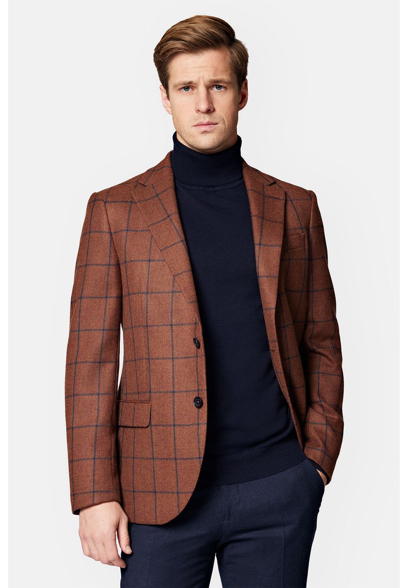 Brązowa marynarka w kratę z teksturowanej tkaniny, z dwoma guzikami, klapami w stylu notch i kieszeniami naszytymi, noszona na granatowym golfie.