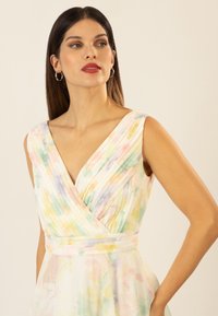 Abito fluido senza maniche in colori pastello con scollatura a V, tessuto plissettato e motivi floreali. Materiale leggero con una texture liscia.