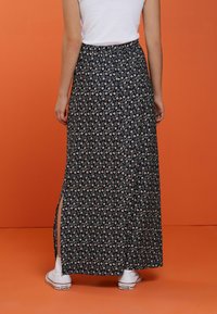 Falda maxi en azul oscuro con un estampado floral, con aberturas laterales y una cinturilla elástica, combinada con zapatillas blancas.