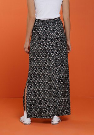 Maxi rok in donkerblauw met een bloemenpatroon, met zijslits en een elastische tailleband, gecombineerd met witte sneakers.