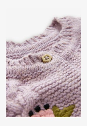 Levandų spalvos megztas audinys su raukšlėta tekstūra, kuriame yra mažas įdegio spalvos gėlės formos mygtukas ir dalinė gėlių siuvinėjimas rožine, juoda ir žalia spalvomis.