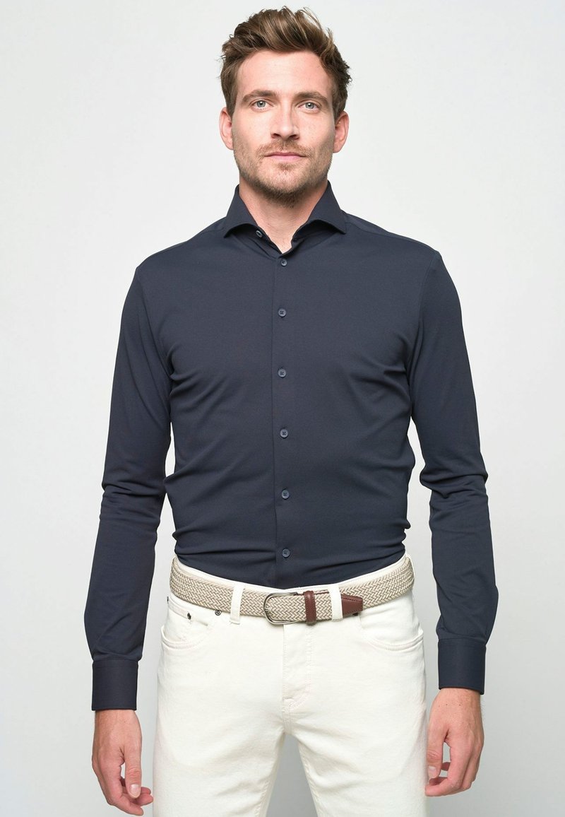 Marineblauw overhemd met lange mouwen en knopen, soepel stof, normale pasvorm, gecombineerd met een geweven beige riem, gedragen met lichte spijkerbroeken.