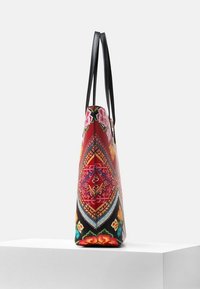 Sac fourre-tout coloré avec motifs floraux, anses noires texturées et forme effilée, fabriqué en tissu durable avec une finition brillante.