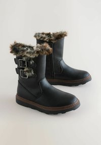 Botas de tobillo negras con ribete de pelo sintético, adornos de doble hebilla y cremallera lateral; suela de goma con textura antideslizante.
