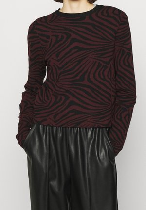 Pull bordeaux avec des rayures noires en zèbre, col rond et manches longues, associé à un pantalon en cuir noir avec des poches latérales.