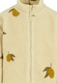 Giacca in fleece, color crema con una texture morbida, presenta motivi di limoni gialli e foglie verdi, e una chiusura a zip frontale.