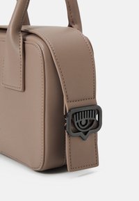 Brun läderhandväska med en elegant rektangulär form, som har en rem med en svart ögonformad spänne och synliga sömnadsdetaljer.