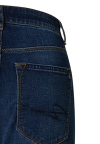 Donkerblauwe denim jeans met een zichtbare achterzak, gele stiksels en een subtiel ontwerpelement nabij de zak. Duidelijke textuur zichtbaar.
